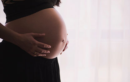 Pregnant torso region with hands on either side standing in front of a billowy white curtain.