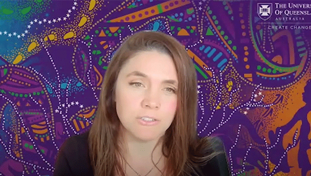 Dr Nicole Hewlett looks straight at the camera in front of a piece of Aboriginal Artwork