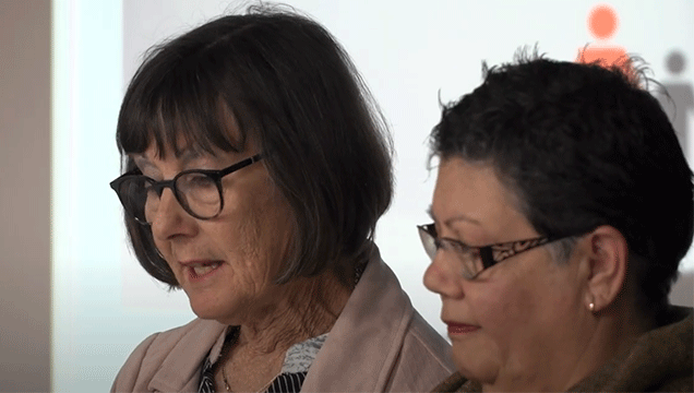 A photo of two women looking addressing an audience