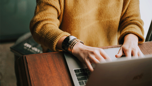 Person wearing yellow jumper typing on their laptop.