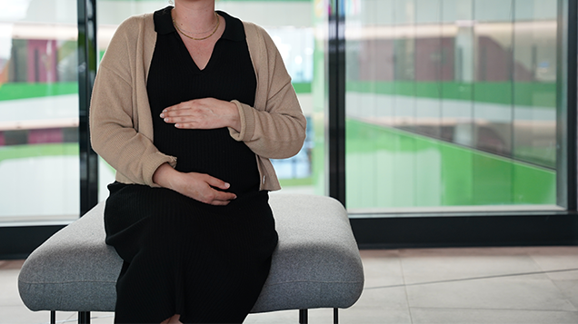 Pregnant mother resting her hands above and below her belly whilst in a seated position.