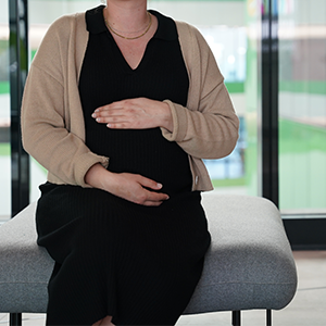 Pregnant mother resting her hands above and below her belly whilst in a seated position.