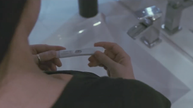 Person holding a positive pregnancy test stick over a sink